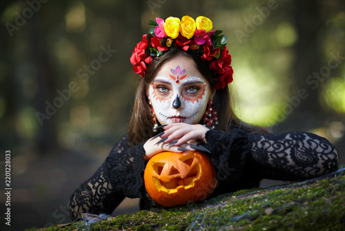 Halloween beauty portrait of young woman with Halloween pumpkin lies on a tree trunk in the forest.