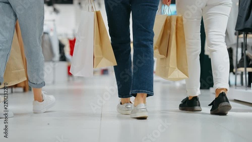 Low-angle view of three women walking through clothing store holding paper shopping bags, concept of movement and modern retail lifestyle