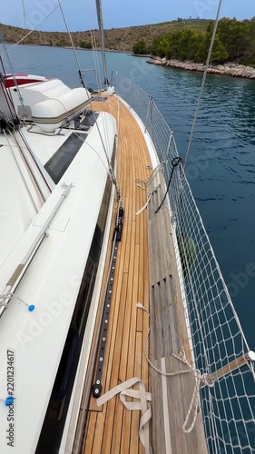 Woman walking along deck toward bow of sailing yacht near Croatian island. Camera tilting up from bare legs reveals boat bow and scenic Mediterranean coastline