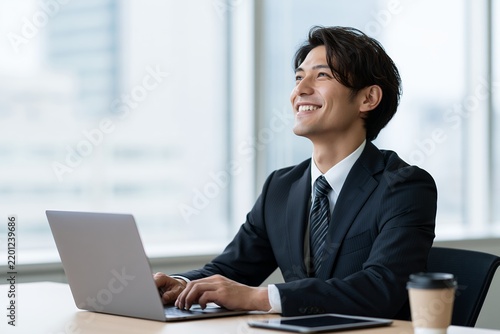 オフィスでパソコン作業する笑顔の日本人男性ビジネスマン未来への希望を感じる