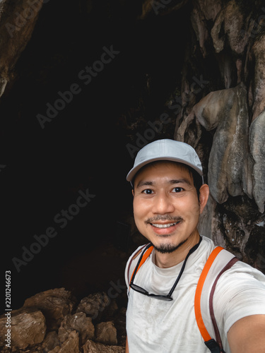 Smiling Asian man takes a selfie inside a dark cave, exploring Southern Thailand.
