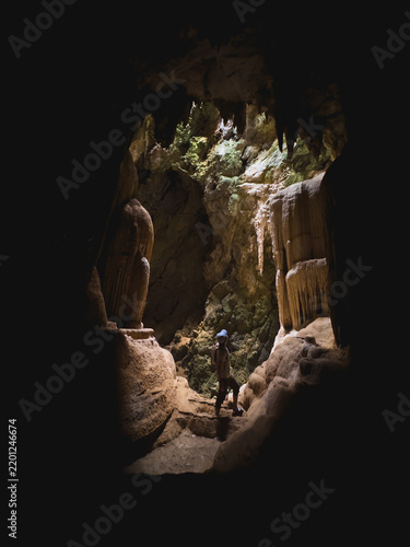 Adventurous Person Exploring Majestic, Naturally Lit Limestone Cave Formations in Southern Thailand.