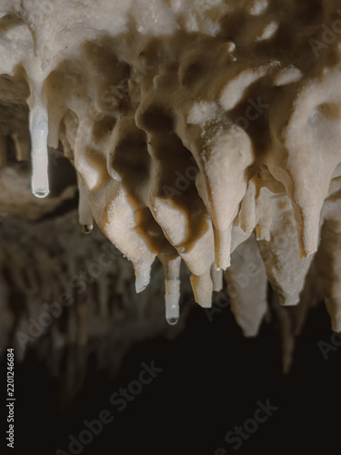 Close-up View of Natural Stalactite Formations with Dripping Water Inside a Dark Cave