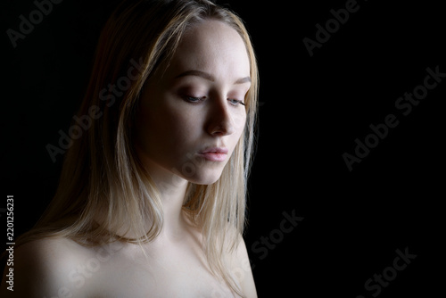 Dramatic portrait of thoughtful blonde woman illuminated by soft directional light.