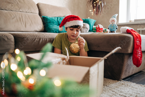 Kid boy decorating Christmas tree put off balls from the box authentic real celebration image lifestyle. Xmas with family children fun at cozy home