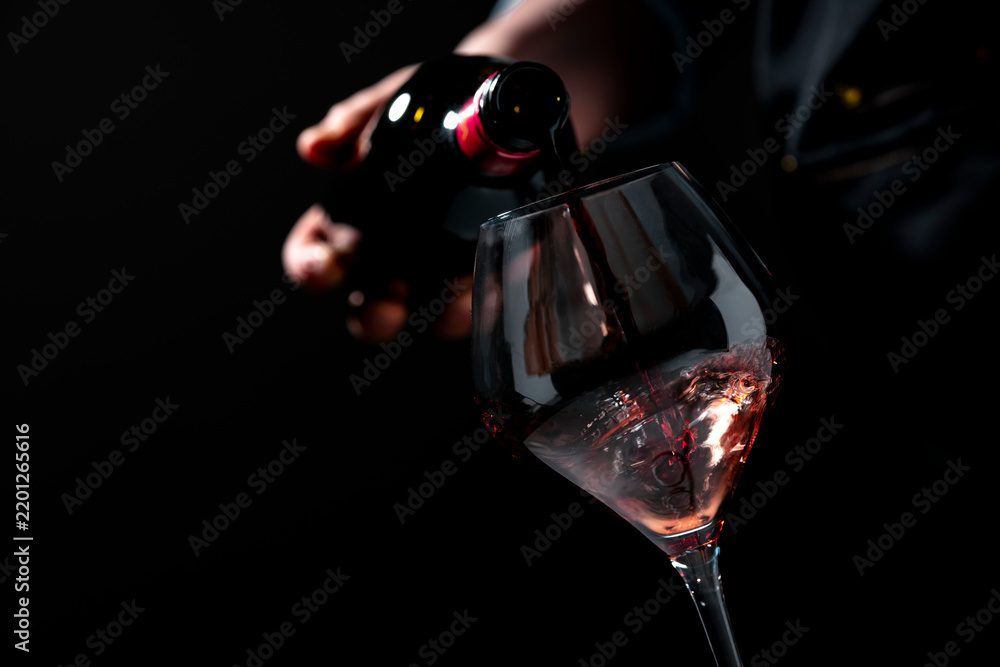Naklejka premium Delicious red wine Merlot in glass from dark bottle — luxury celebration concept. Expert sommelier in apron serving alcoholic beverage. Premium restaurant hospitality, gourmet food pairing.