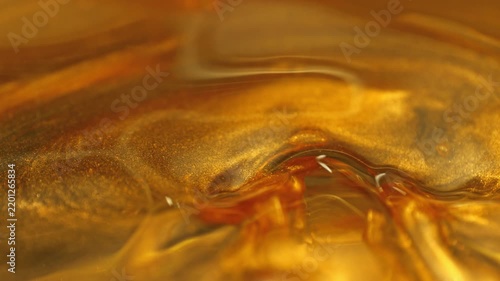 Super Slow Motion Shot of Swirling Golden Glittering Oil in Water at 1000fps.