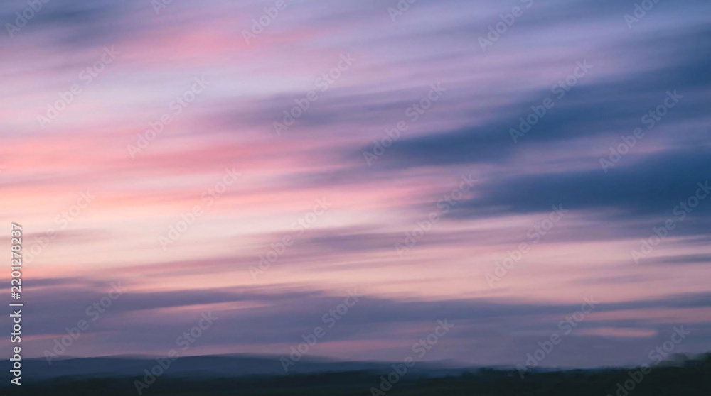 Fototapeta premium Soft pastel sunset sky with wispy clouds in pink and purple hues over a silhouetted landscape, serene atmosphere