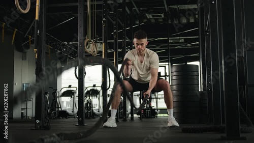 Powerful Caucasian muscular man athlete training with battle ropes in fitness gym sportsman bodybuilder male performing intense cardio workout physical strength exercise trainer bodybuilding indoors