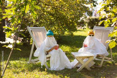two kids in Halloween ghost costumes Wearing bright hats and black glasses, they drink lemonade in the park. Halloween party
