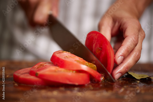 Hand slicing fresh red tomato on cutting board