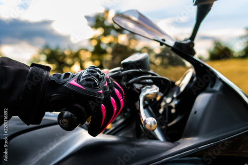 Biker's hand wearing pink and black protective glove gripping motorcycle handlebar