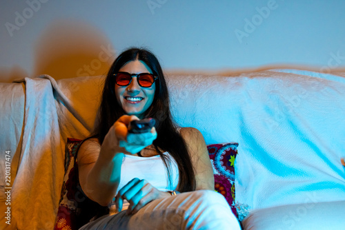 Woman wearing blue light blocking glasses watching tv with remote control