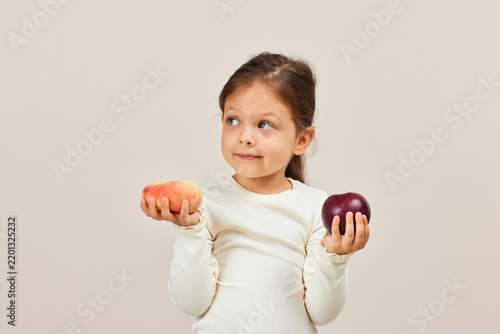 Little girl choosing between peach and red apple
