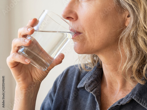 Close-up of a mature woman drinking water from a clear glass, illustrating daily hydration, healthy aging, and natural wellness routines.