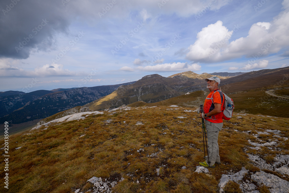Obraz premium a 75-year-old man hiking in the mountains with poles, a backpack, and mountain gear on a beautiful September day