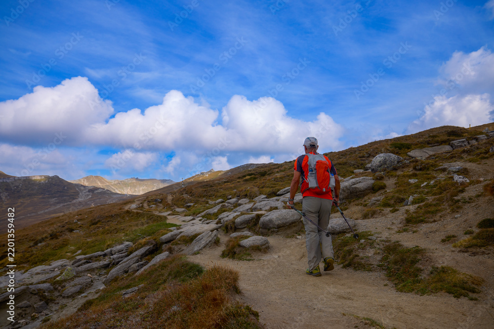 Obraz premium a 75-year-old man hiking in the mountains with poles, a backpack, and mountain gear on a beautiful September day