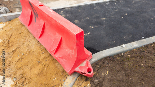 Canvastavla Red temporary safety barrier placed near fresh asphalt during road construction,