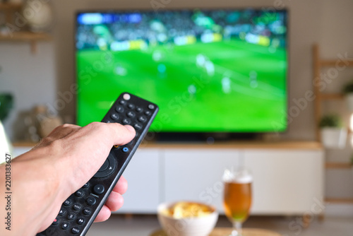 Hand holding remote control changing tv channel during soccer game