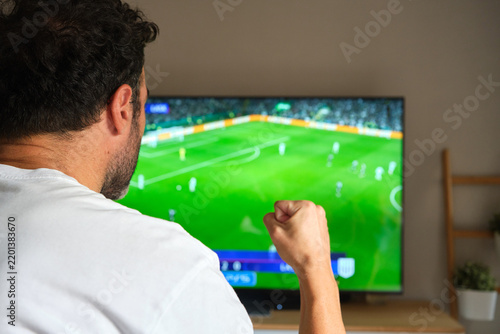 unrecognizable man watching a soccer match on television and celebrating a goal.