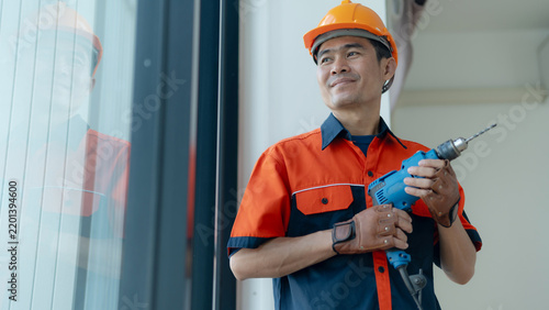 Professional construction worker holding a power drill while wearing a safety helmet and uniform