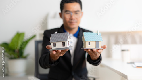 Professional real estate agent holding two miniature house models for property comparison