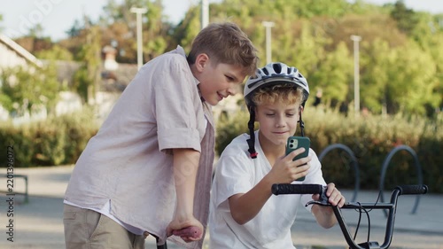 Two 10 Year Old Boys Looking at Smartphone Screen Outdoors in Park