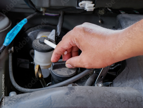 a mechanic's hand holding a cigarette while working on an open car engine in a garage. Suitable for editorial articles, workplace safety campaigns, health risk presentations, and automotive service to