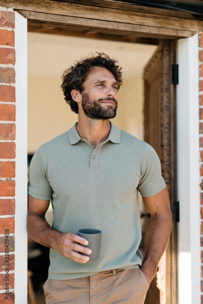 Fototapeta premium Man standing in a doorway holding a mug and looking away for casual morning portrait and peaceful home lifestyle background