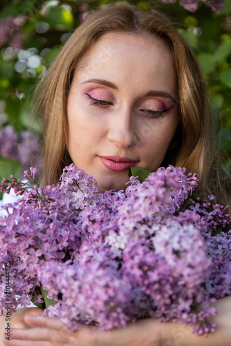 Woman in elegant purple dress posing in blooming spring lilac garden
