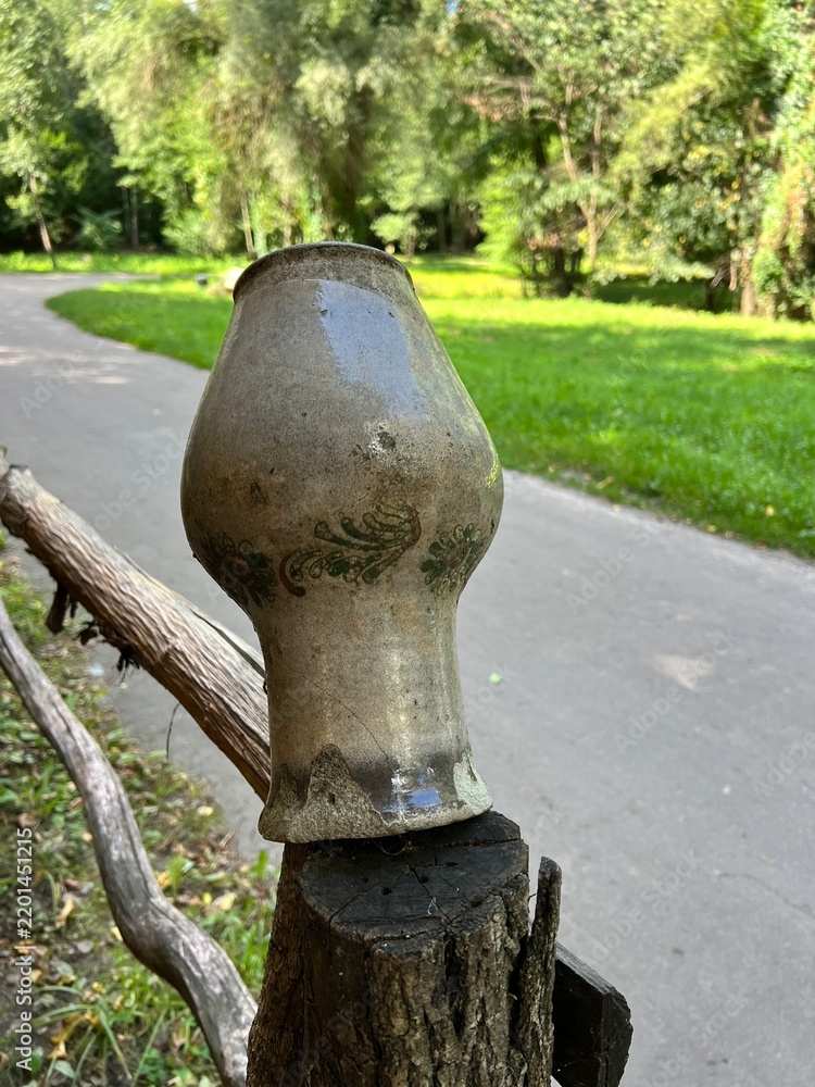 Obraz premium Old clay pot displayed on a rustic wooden post beside a green path in a peaceful summer park
