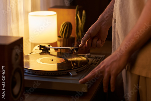 Young adult Caucasian man placing stylus needle on vinyl record turntable at home. Closeup suitable for music streaming campaigns and lifestyle marketing