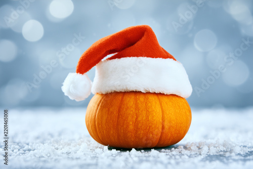 Pumpkin wearing santa hat on snowy surface with blurred background