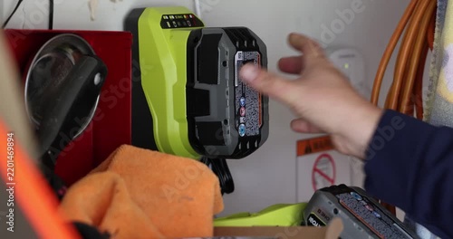Power Tool Battery Charging Process, A person inserts a lithium ion battery pack into a wall mounted charger in a workshop setting to replenish power for cordless construction equipment
