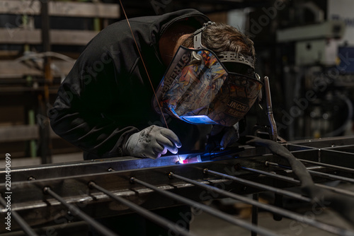 фотографія Welder in a helmet welding a steel framework on a workbench