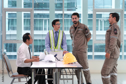 Construction worker engineer safety vest hard hat workplace discussion with diverse construction workers and engineer reviewing plans around table modern building, showing professional teamwork