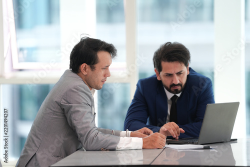 Business meeting with two male colleagues reviewing laptop information in modern office, showing focused teamwork, discussion, and professional collaboration