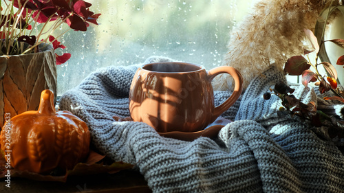 Autumn vibes. Tea time or coffee break. Mug of hot steaming drink on windowsill in cozy interior, raining outside. Warm cozy fall mood. 