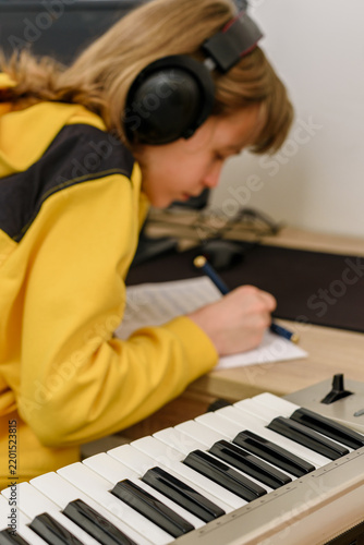 фотографія Teenage boy sitting at desk with electronic keyboard, wearing headphones and wri