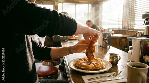 Person pouring maple syrup onto delicious breakfast waffles.