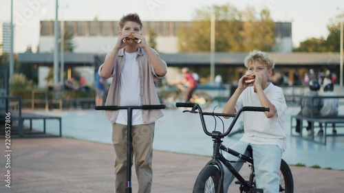 Two 10 Year Old Boys Eating Burgers outdoors in Skate Park