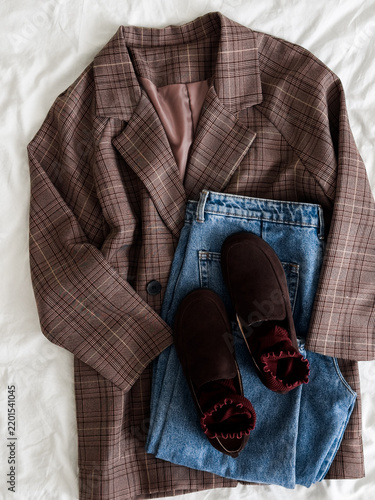 A checkered blazer, blue jeans, brown suede loafers on a light background, top view. Comfortable women's casual clothing