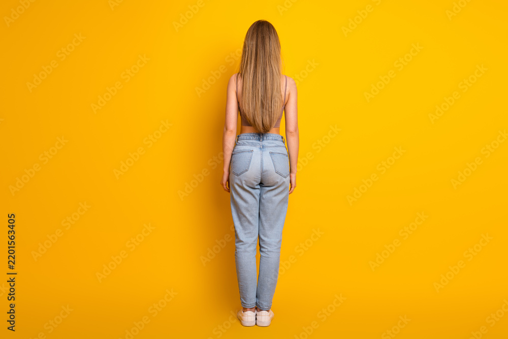 Obraz premium Portrait of a stylish young woman in casual outfit posing against a vibrant yellow background in relaxed stance