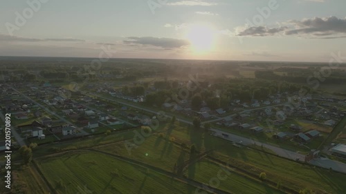Drone footage, aerial view of a small rural village among green fields at sunset. Harmony of a simple suburban life.