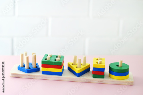 Colorful wooden shape sorting puzzle on a pink table, supporting neurodevelopment and cognitive skills. Ideal for educational resources, preschool ads, toy catalogs, and learning websites.