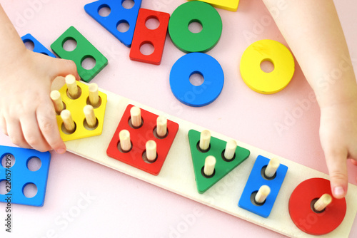 Child’s hands playing with a colorful wooden shape sorting puzzle on a table. Ideal for educational materials, preschool promotions, toy store ads, parenting blogs, and learning posters.