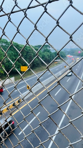View of Highway Traffic Seen Through Wire Chain Link Fence Overpass