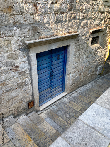 Weathered blue wooden door is set into a rustic stone wall along a stepped alleyway