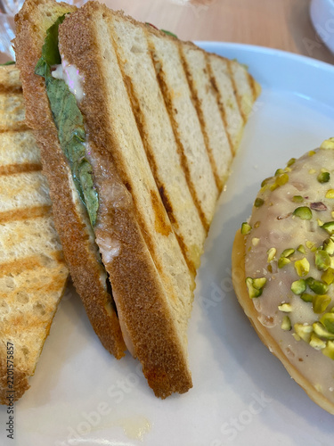 Grilled sandwich halves served on a white plate next to a glazed pistachio donut
