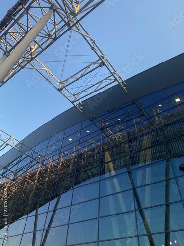 Low-angle view of a modern glass building facade reflecting its external steel truss structure under a clear blue sky
